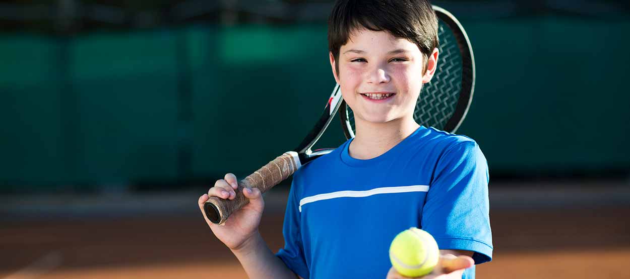 Kind mit Tennisschläger und Ball lächelt den Betrachter an
